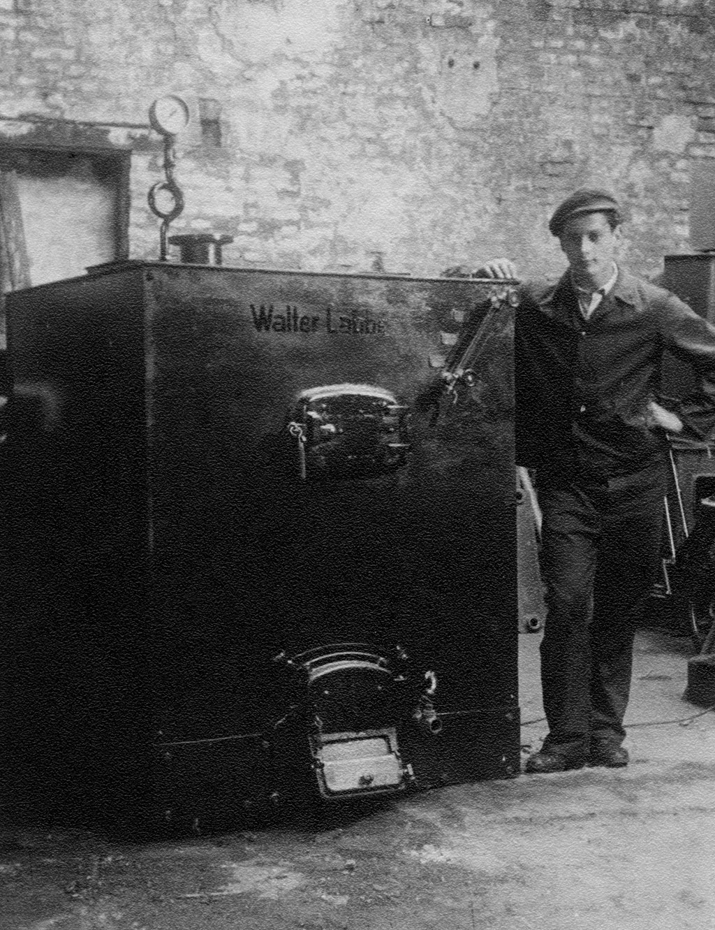 Schwarzweißfoto: Arbeiter lehnt neben großem Industrie-Heizkessel „Walter Labbé“ in einer Werkstatt.